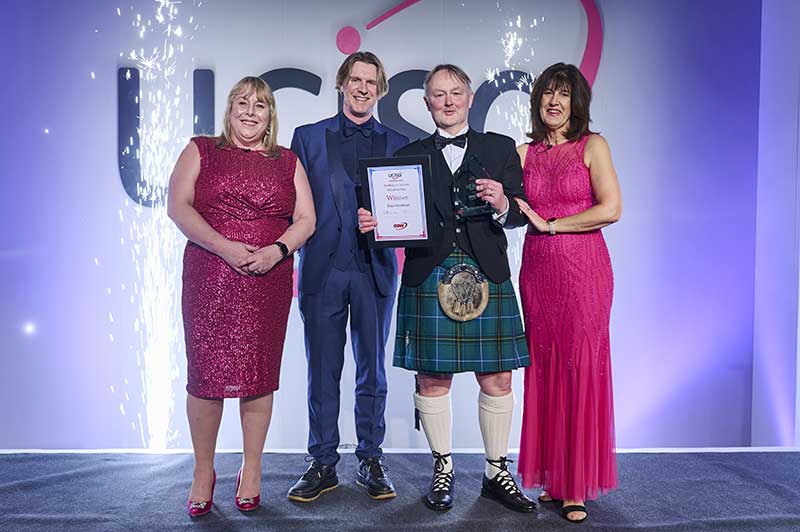 4 people of a stage one in a kilt holding an award and certificate in a frame