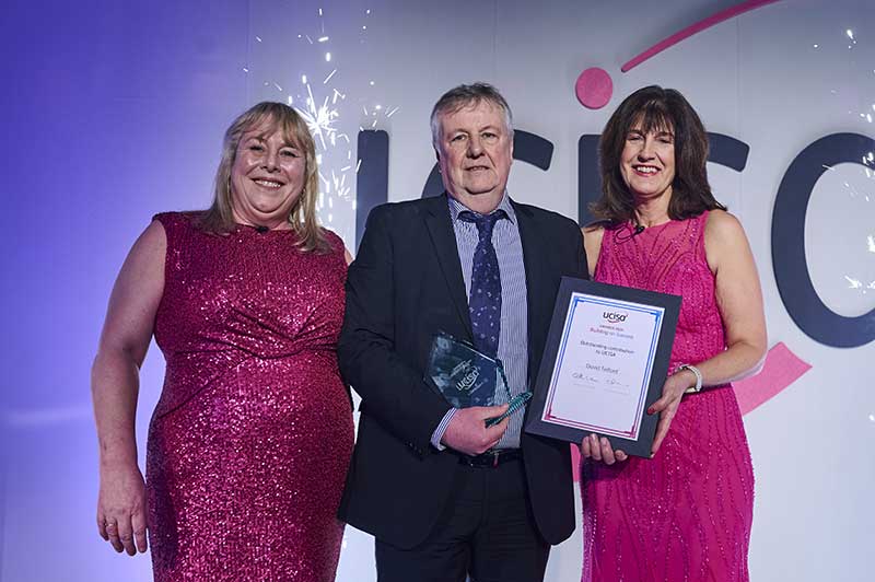 3 people on a stage one holding an award and certificate in a frame