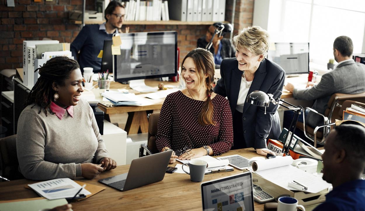 group of men and women in a office setting three women in the forefront smiling at each other