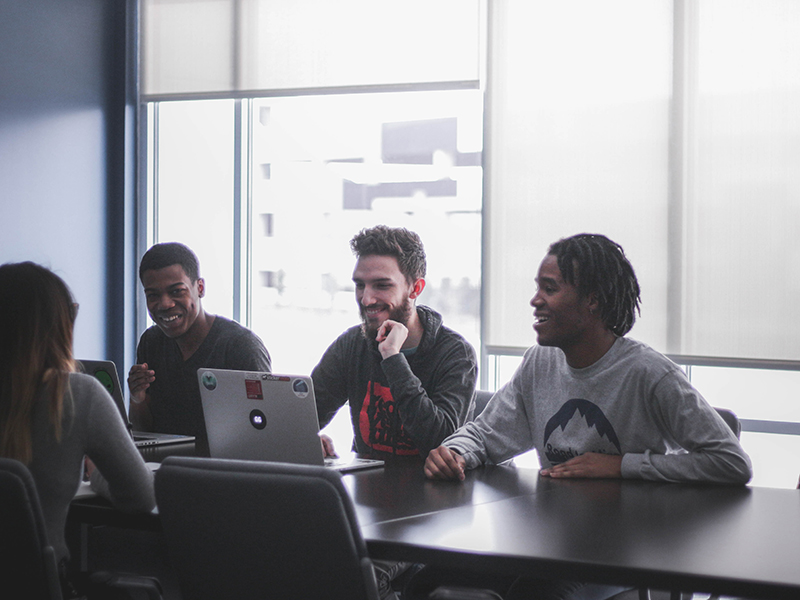 four people sat around a laptop on a table