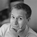 black and white head and shoulder shot of a man with his hand on his chin smiling 