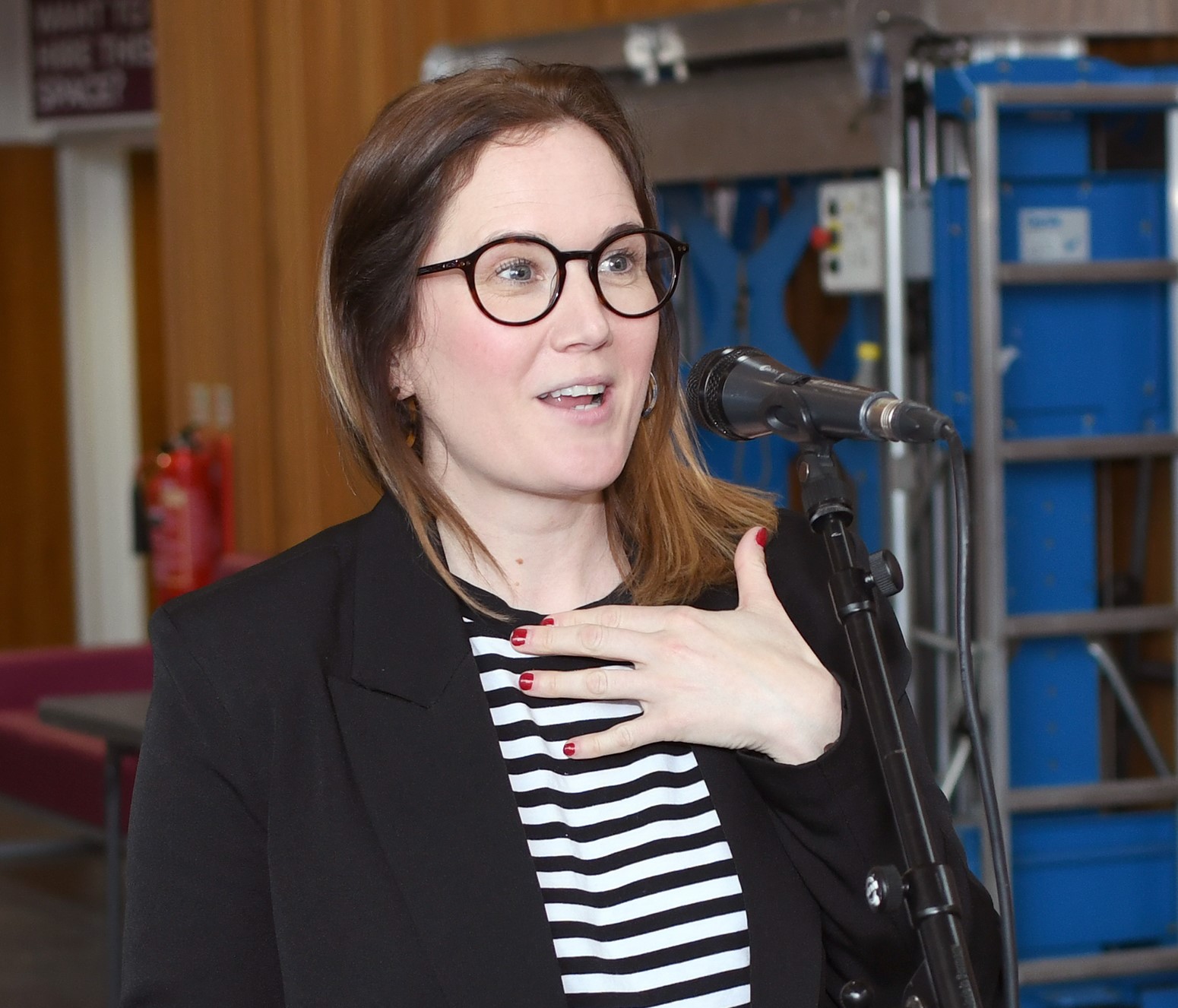 Photo of Sarah in a black blazer talking into a microphone