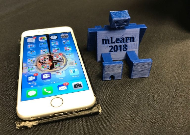 Colour photograph of a 3D-printed robot phone holder, plus iPhone 6s
