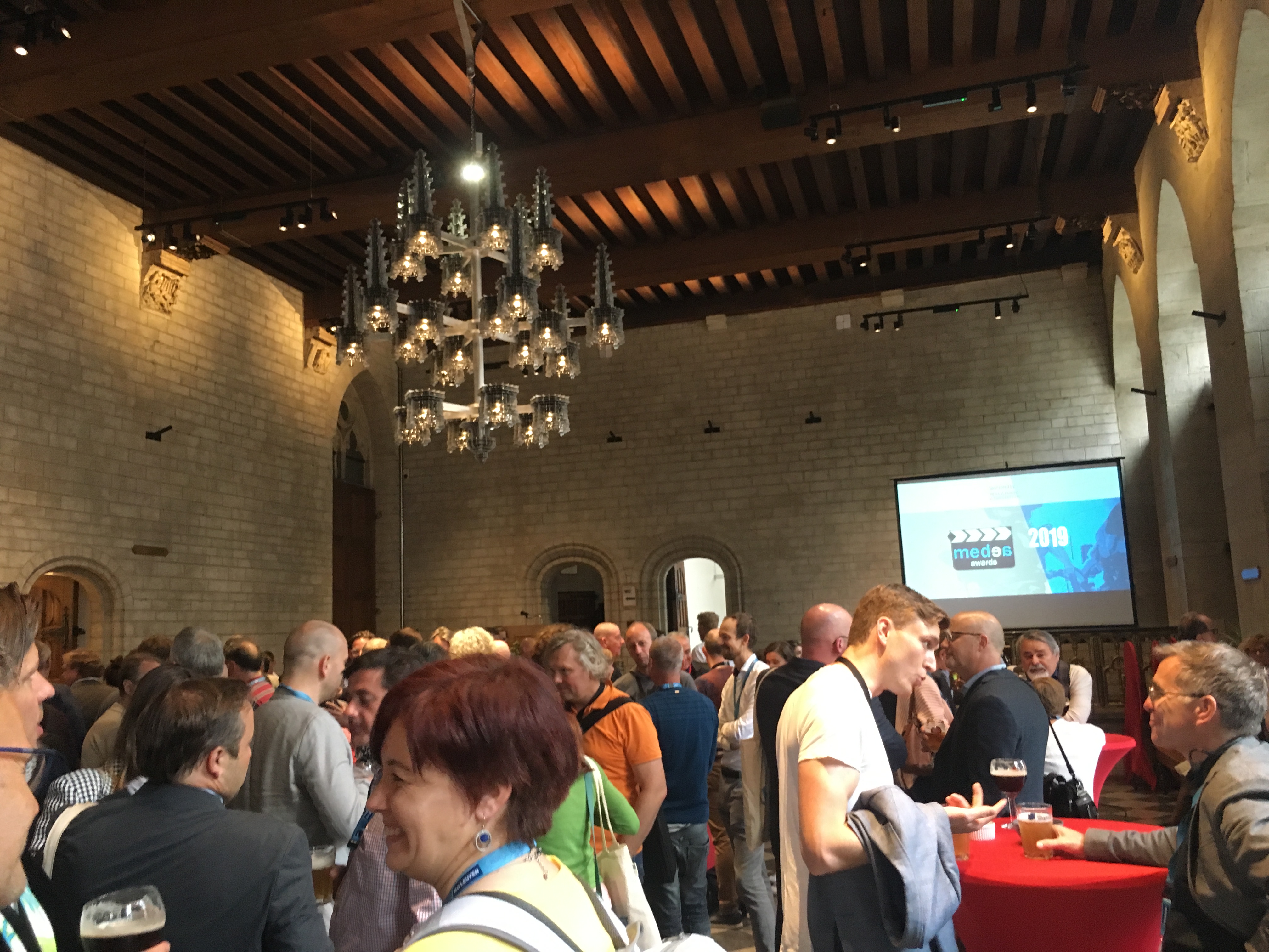 Colour photograph of people taking part in the Medea awards presentation in a high ceiling room with beams