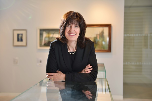 woman in a black suit with her arms folder leaning over a glass bench smiling